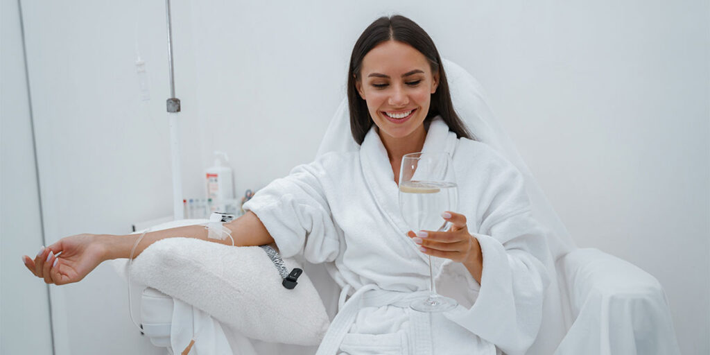 Woman in white bathrobe drink water during medical procedure in beauty clinic. High quality photo.